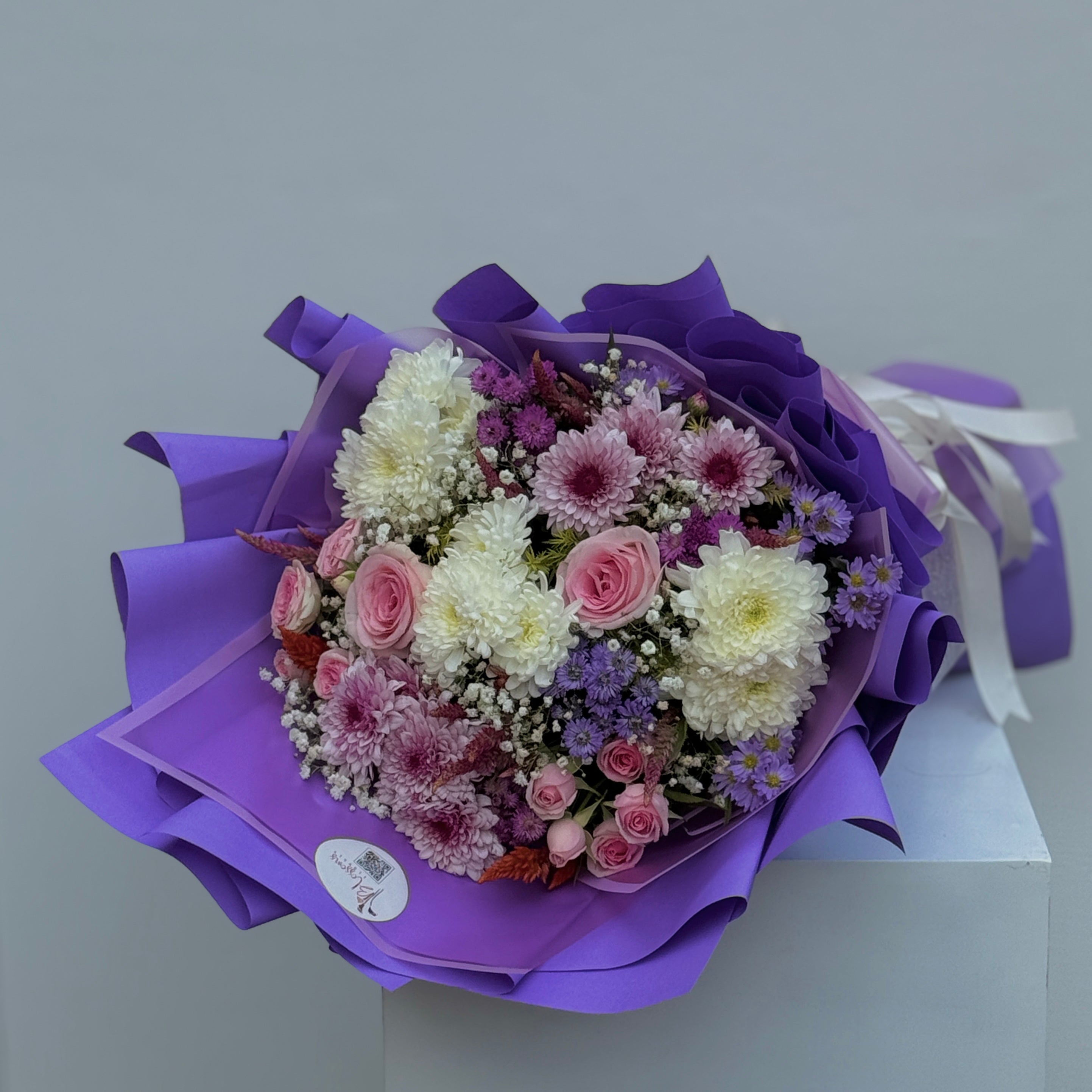 Bouquet of flowers wrapped in purple paper on a light gray background