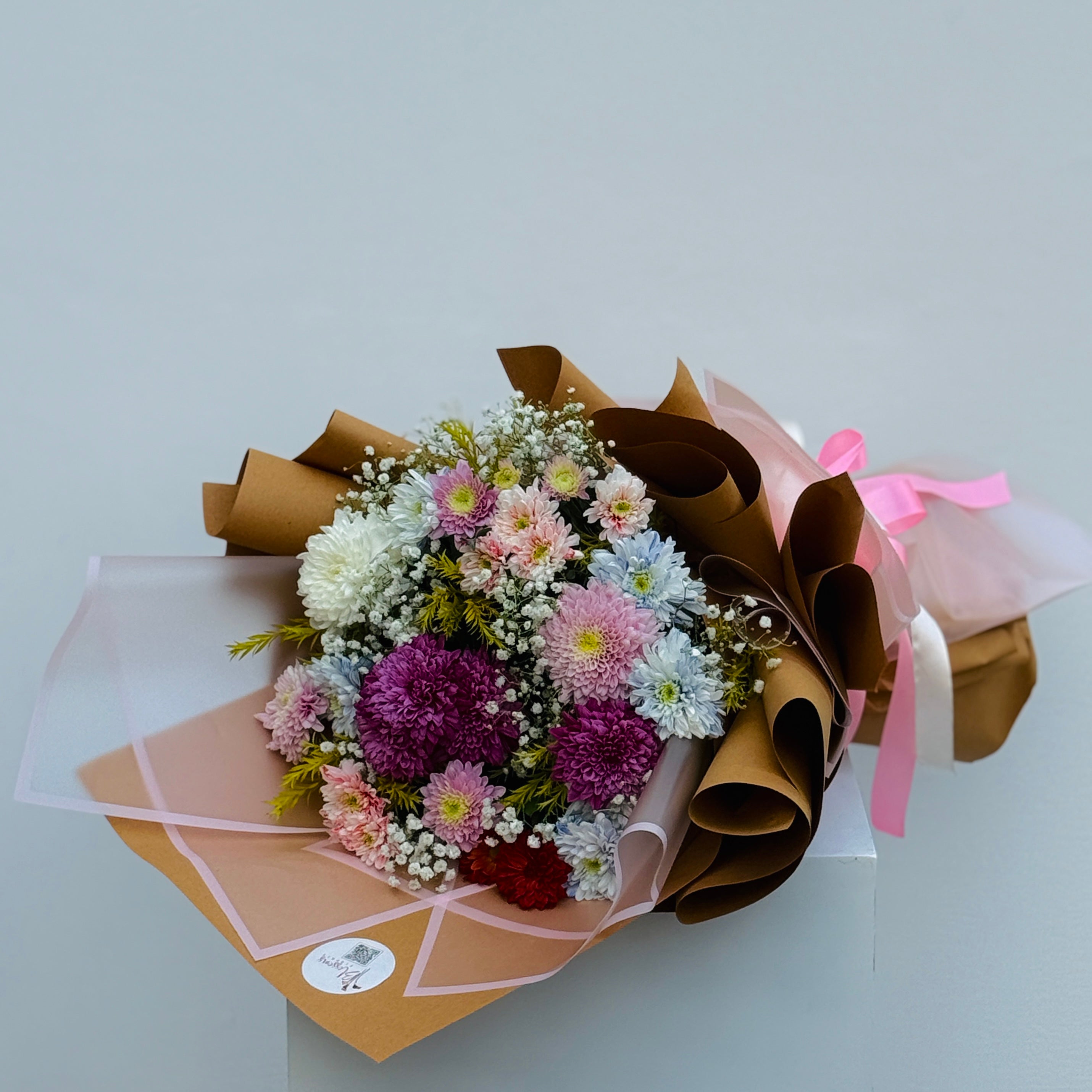 Bouquet of chrysanthemums wrapped in brown paper with pink ribbons on a light gray background