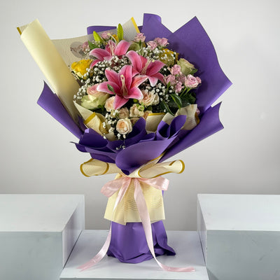 Bouquet of flowers wrapped in purple paper with a pink ribbon on a white surface.