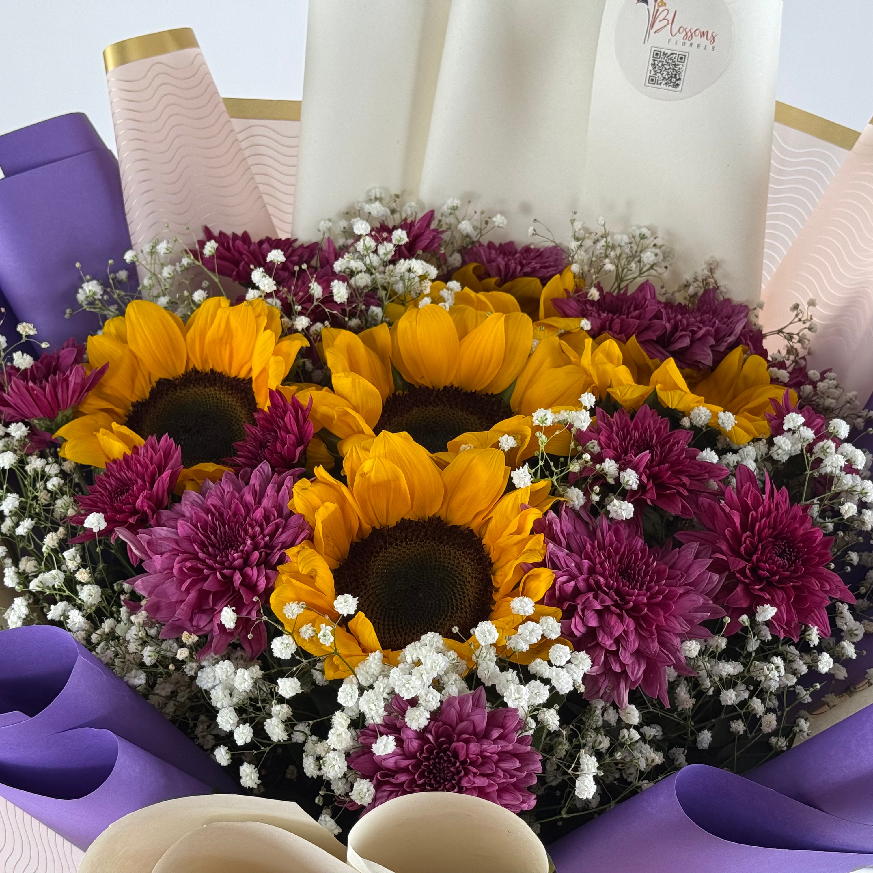 Bouquet of sunflowers, purple flowers, and white baby's breath with a visible brand logo.