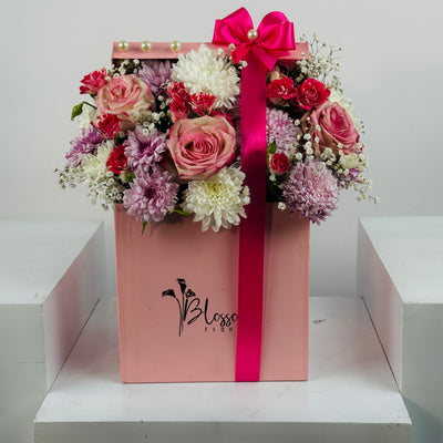 Floral arrangement in a pink box with a visible brand logo on a white background