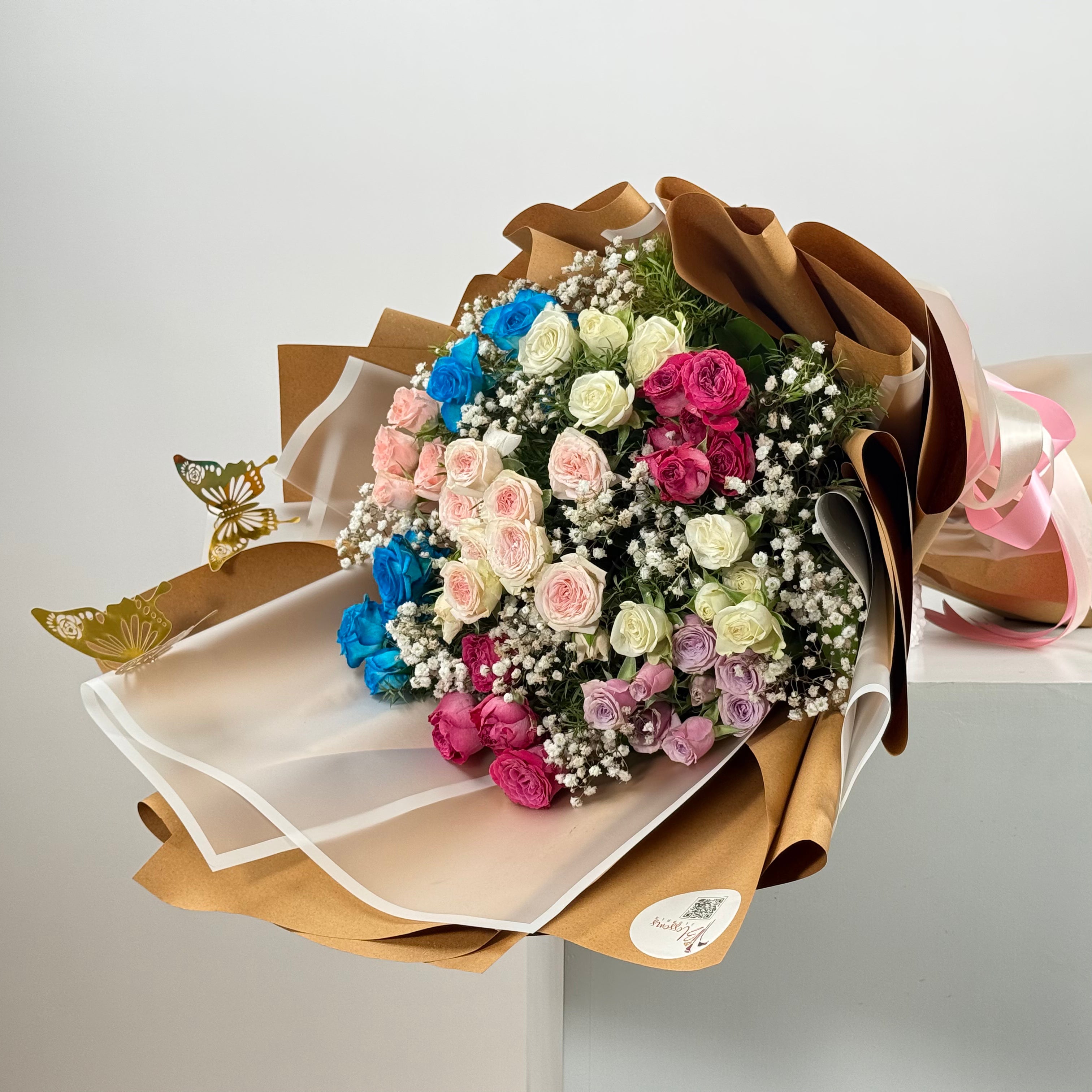 Bouquet of multicolored spray roses wrapped in brown paper on a white surface.