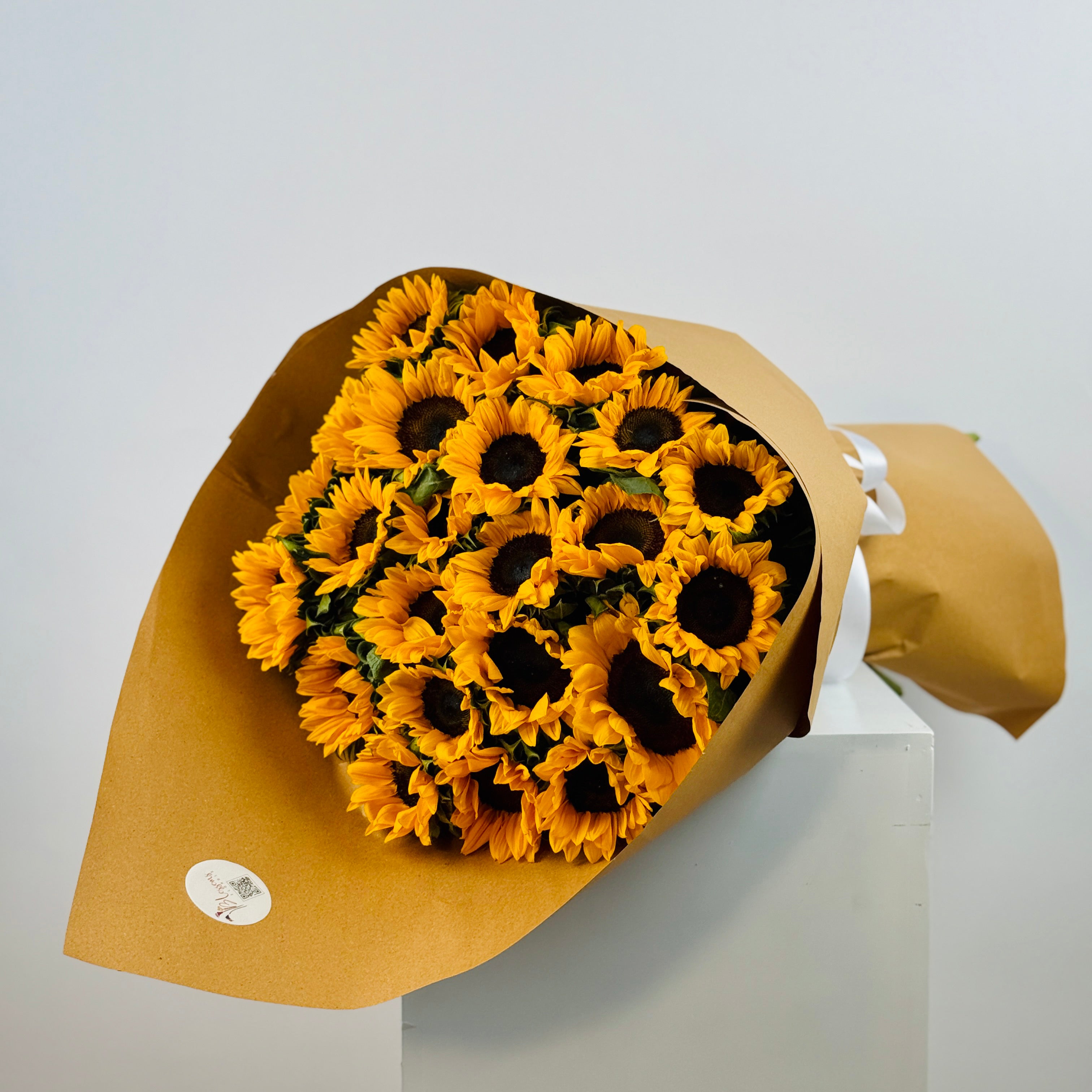 Bouquet of sunflowers wrapped in brown paper on a white surface with a light gray background
