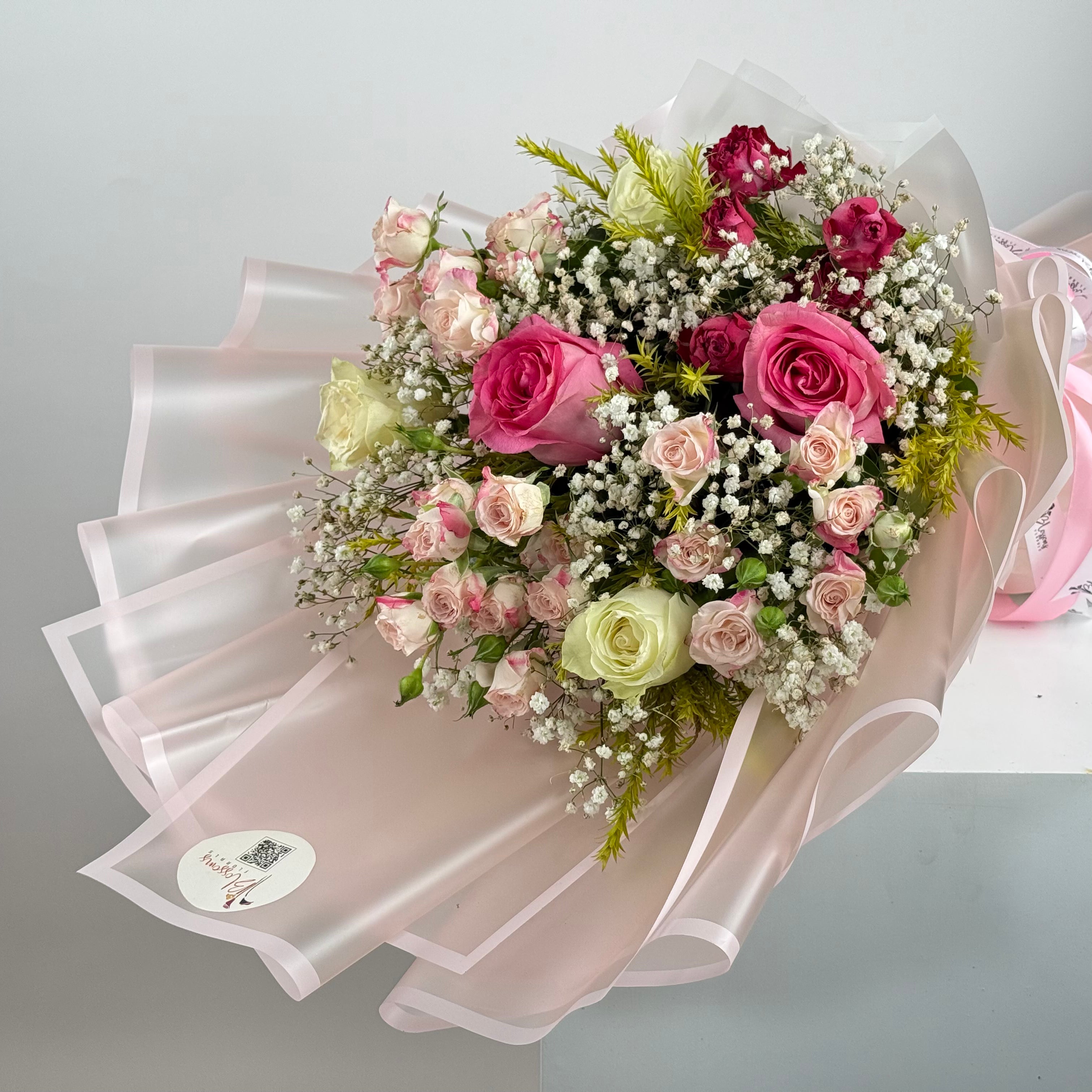 Bouquet of pink and white flowers with a decorative pink ribbon on a light gray background